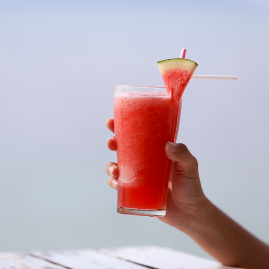 Glass of red watermelon water with a wedge of watermelon on the side of the glass